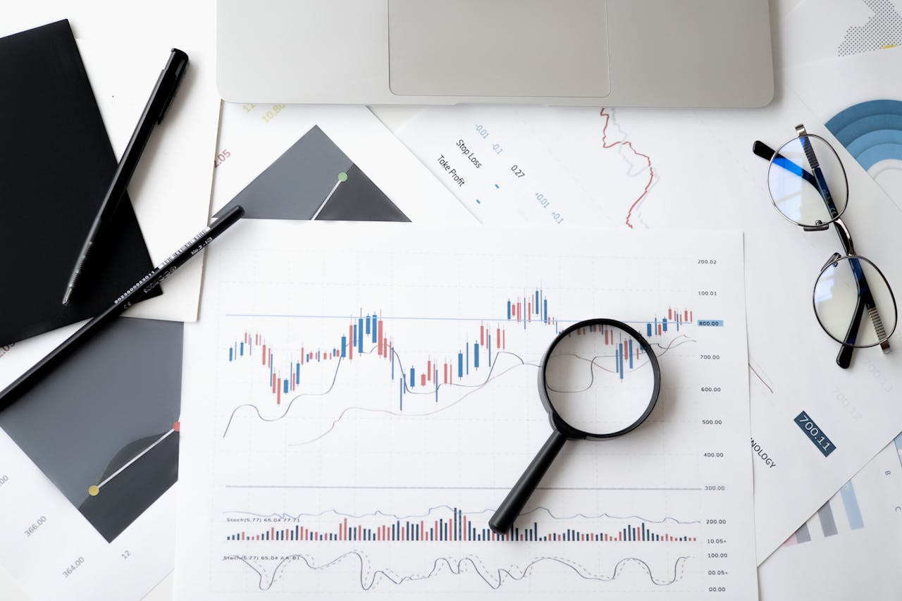 about-02 Flat lay of stock market analysis documents with magnifying glass, pens, and glasses.