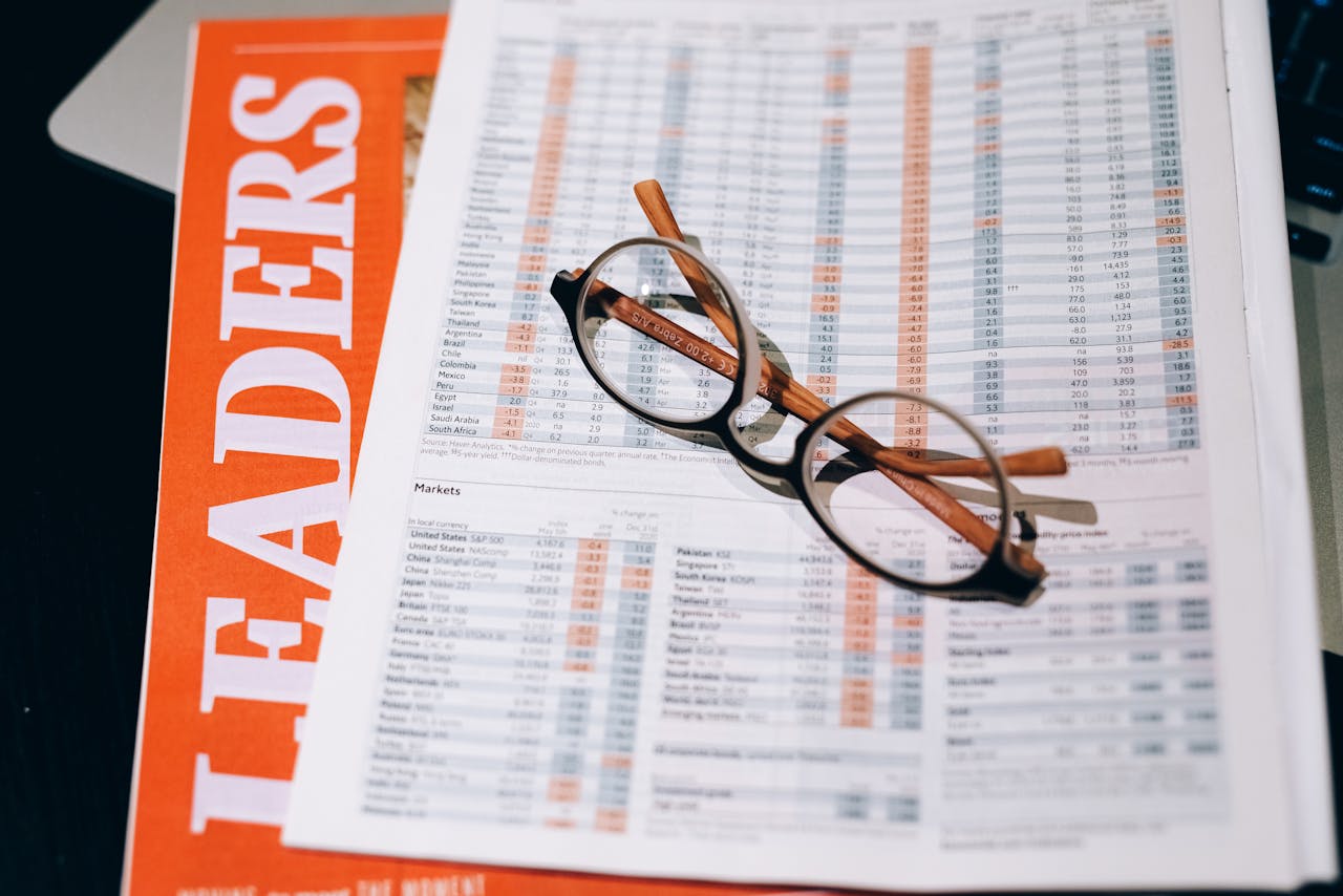 ours-journey A pair of eyeglasses resting on a financial document and magazine with bold headline "LEADERS" in focus.